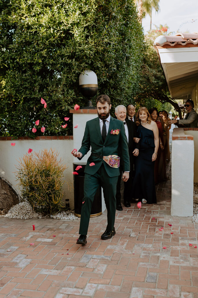 groomsman tosses flower petals from iridescent fanny pack down ceremony aisle 