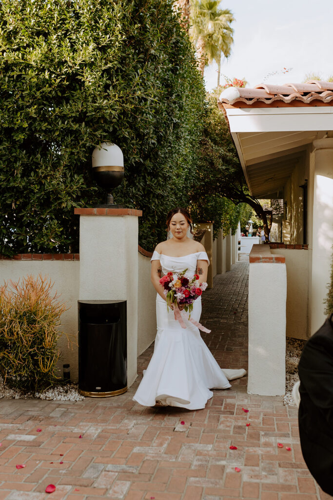 bride in minimalist off shoulder wedding dress and colorful bridal bouquet walks down ceremony aisle