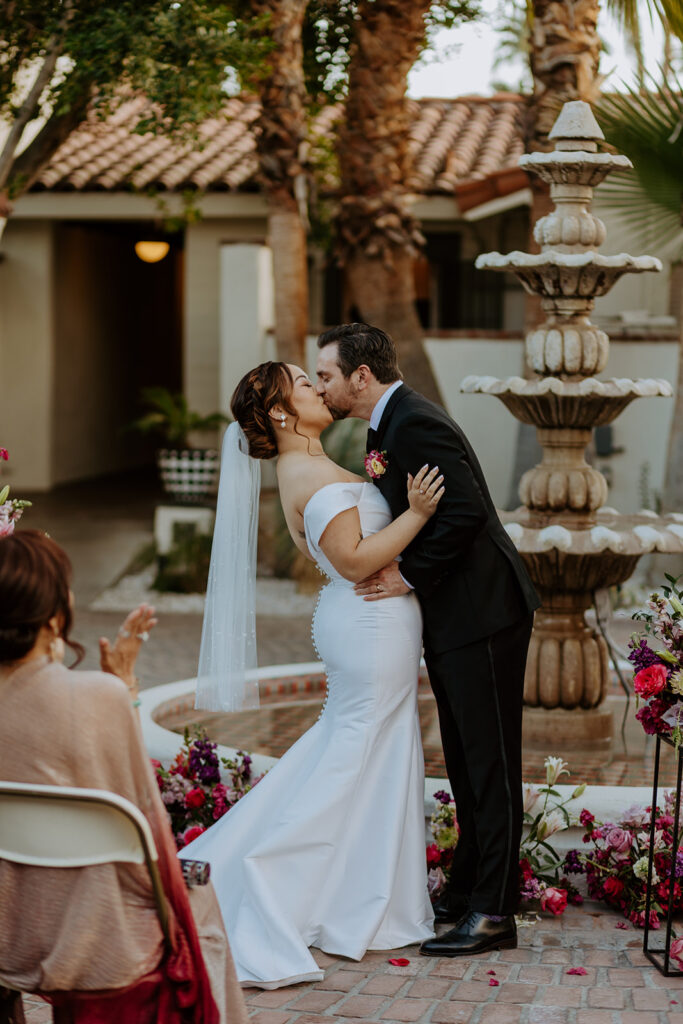bride and groom first kiss during colorful wedding ceremony in front of fountain at Villa Royal Palm Springs