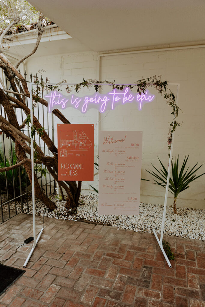 custom neon sign reading "this is going to be epic" hanging above mid-century inspired wedding welcome signs