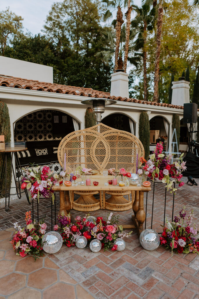 double rattan chairs at sweetheart table for colorful and eclectic pool side wedding reception with disco ball decor at Villa Royale Palm Springs