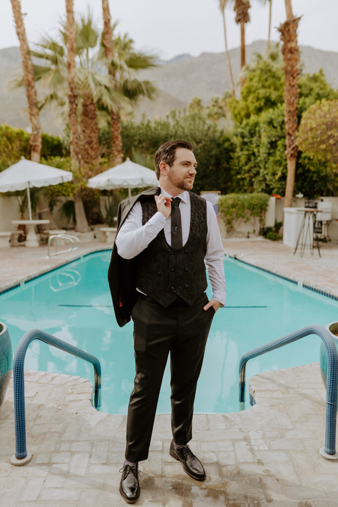 groom in black suit stands by pool side