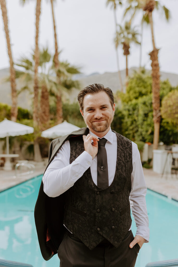groom in black suit stands by pool side