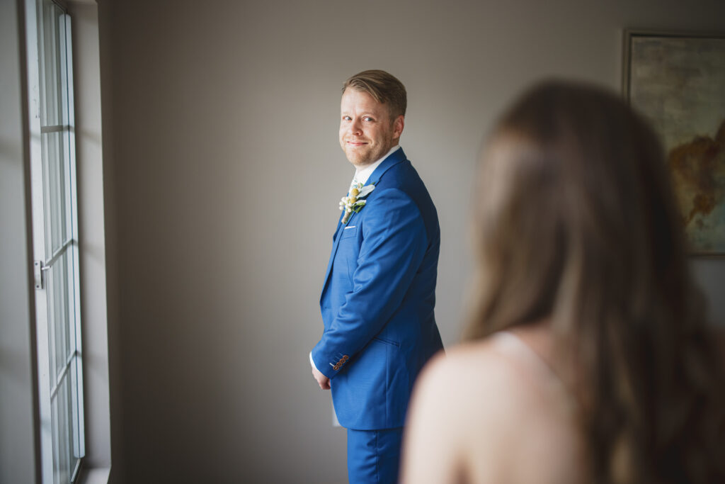 groom in blue suit and billy ball boutonniere has first look with bride in lace vneck wedding dress with tiered skirt