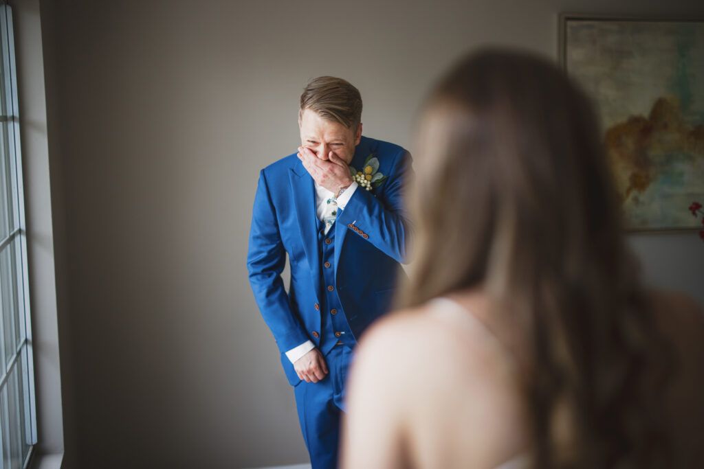 emotional groom in blue suit and billy ball boutonniere has first look with bride in lace vneck wedding dress with tiered skirt