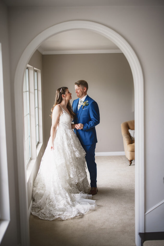 groom in blue suit and billy ball boutonniere has first look with bride in lace vneck wedding dress with tiered skirt