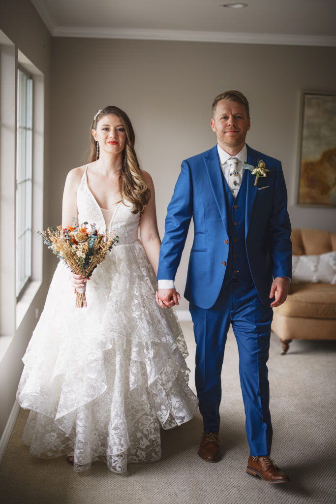 groom in blue suit and billy ball boutonniere with bride in lace vneck wedding dress with tiered skirt and dried floral bouquet
