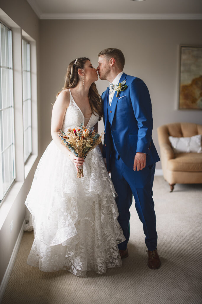 groom in blue suit and billy ball boutonniere with bride in lace vneck wedding dress with tiered skirt and dried floral bouquet