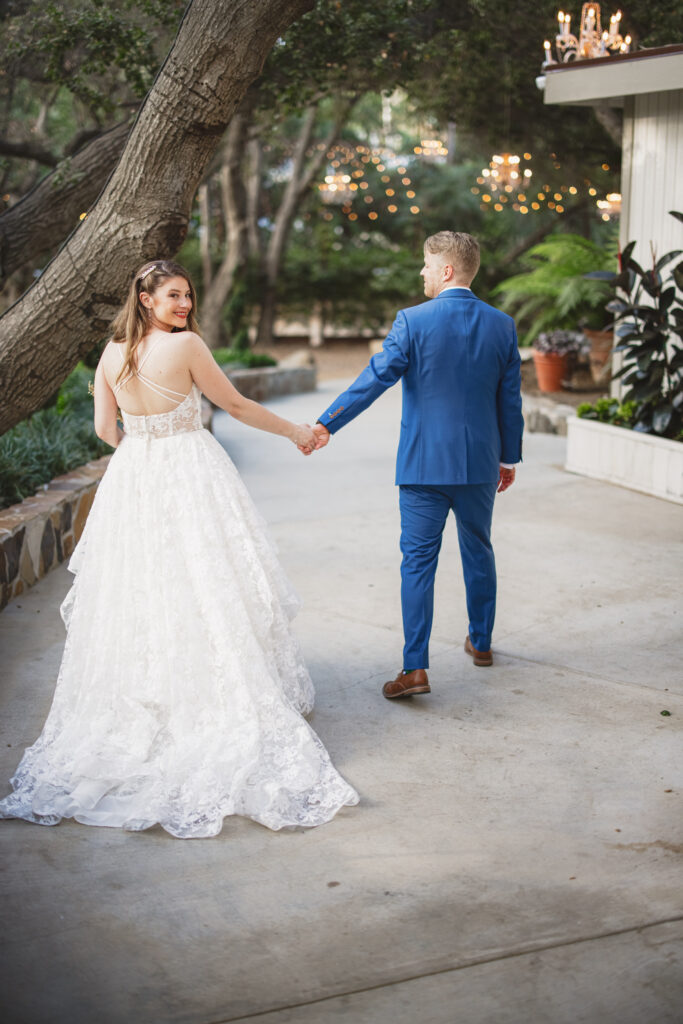 bride in lace deep vneck wedding dress with tiered skirt and groom in blue suit with billy ball boutonniere 