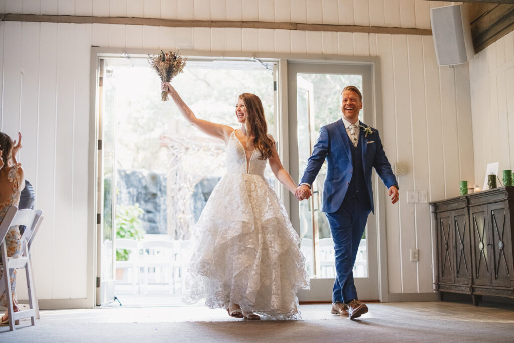 bride in tiered lace wedding dress with groom in blue suit grand entrance for wedding reception at the Oak Room at Calalmigos Ranch
