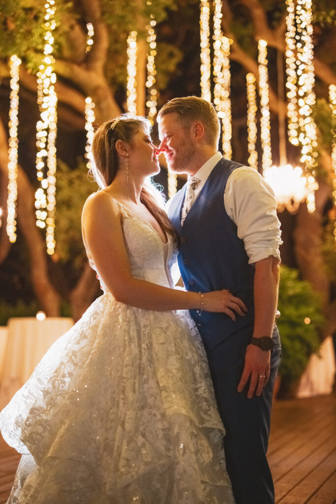 bride in tiered lace wedding dress with groom in blue stand outside with glowing tree lights at Calamigos Ranch