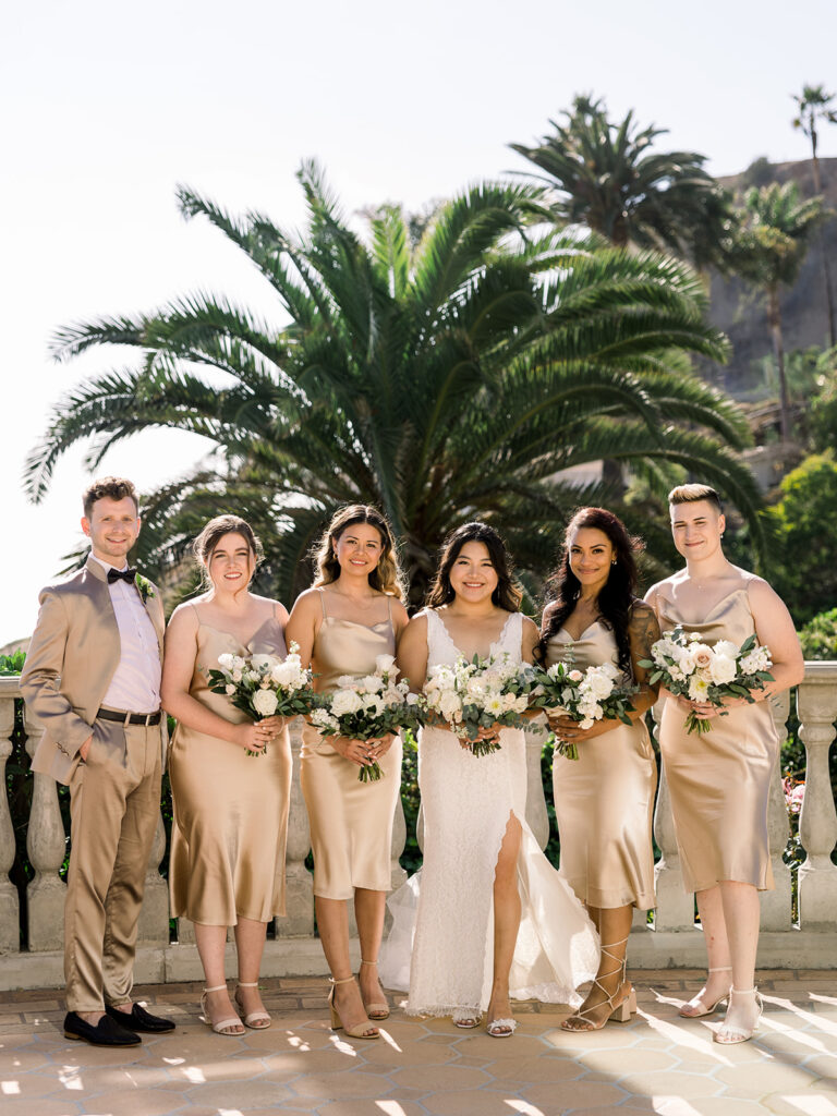 bride in deep v lace wedding dress with leg slit standing with wedding party in Champagne colored suits and dresses