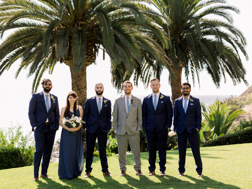 groom in light grey suit with blue tie walks with wedding party in navy blue suits and dress at Bel-Air Bay Club