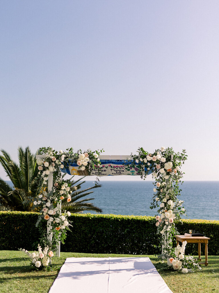 Jewish wedding ceremony chuppah with timeless wedding colors of green, blue and white mixed with soft pink floral arrangements at Bel-Air Bay Club