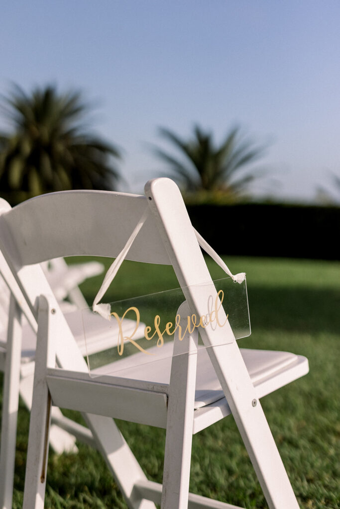 white wedding ceremony chair with clear acrylic sign reading "reserved" hanging on end