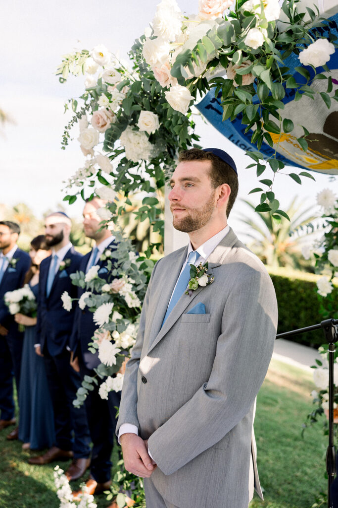 Groom in light grey suit with blue tie during Jewish wedding ceremony