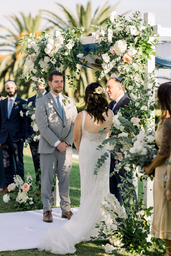 groom in light blue suit and blue tie looks at bride during Jewish wedding ceremony at Bel Air Bay Club 