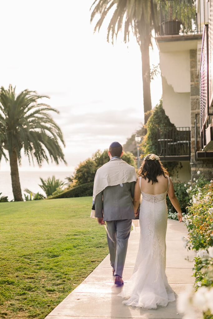 bride in deep v neck lace wedding dress with leg opening walks with groom in light grey suit with blue tie after wedding ceremony at Bel Air Bay Club