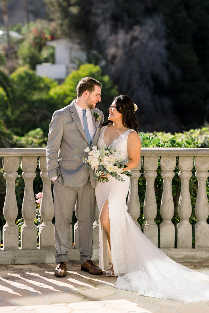 bride in deep v-neck lace dress with leg opening and long train stands with groom in light grey suit and blue tie at Bel Air Bay Club