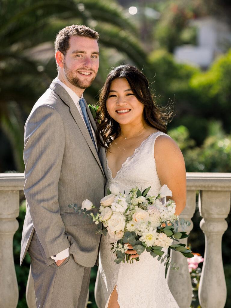 bride in deep v-neck lace dress with leg opening and long train stands with groom in light grey suit and blue tie at Bel Air Bay Club