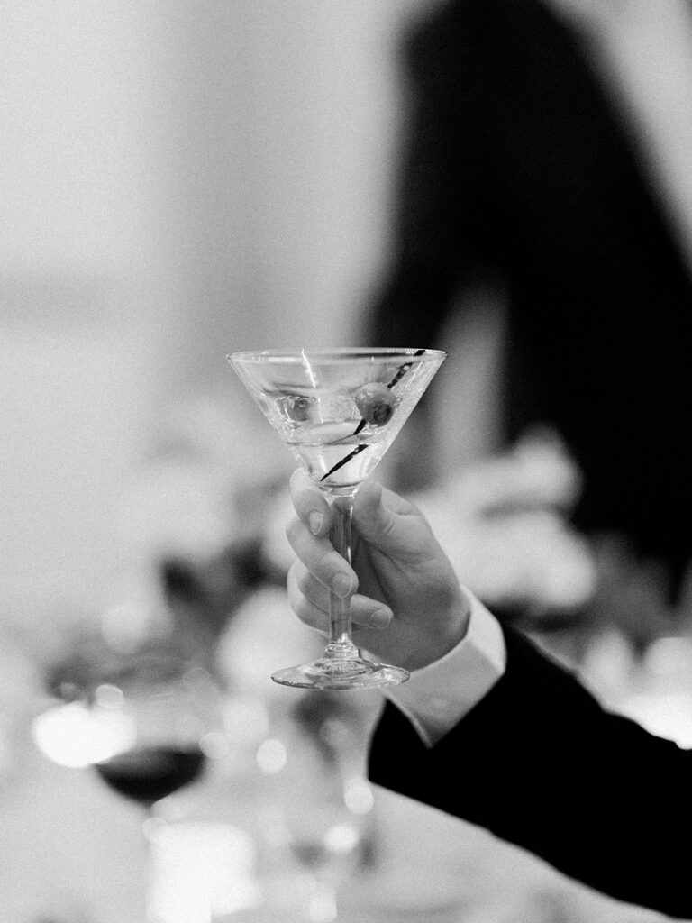 black and white photo of guest holding up Manhattan cocktail in cheers