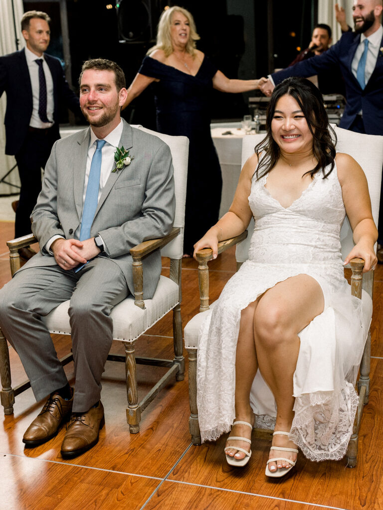 bride and groom sitting in chairs for the horah dance during their wedding reception at Bel Air Bay Club