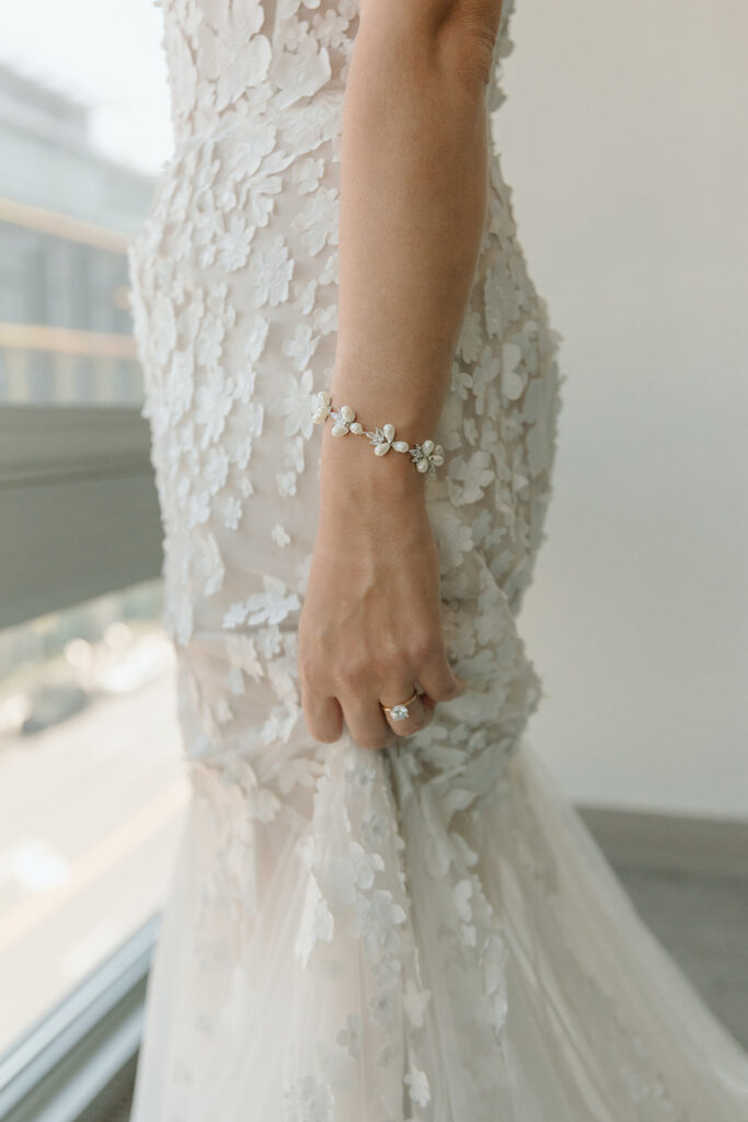 bride getting into strapless wedding dress with 3d floral appliqué while wearing pearl bracelet 