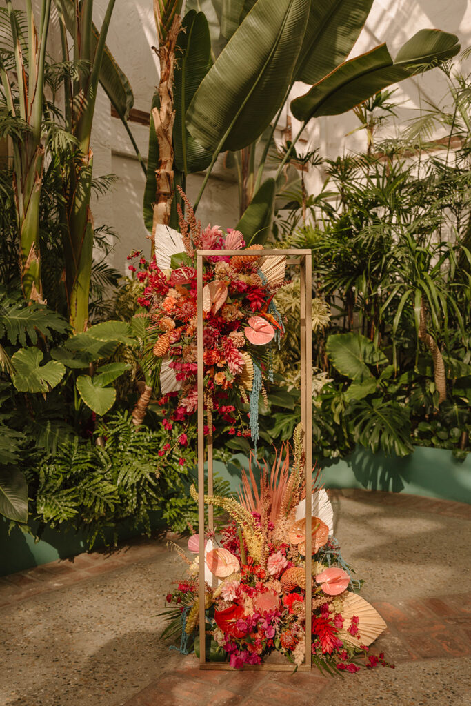 wedding ceremony at Valentine DTLA with pink tropical floral arrangements on top of gold frame stands with a sofreh aghd table