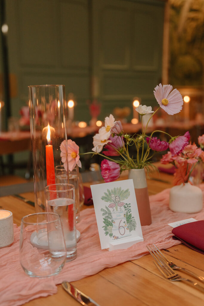 wedding reception at Valentine with pink tropical themed floral arrangements using a mix of dried and real flowers and pink table runner and unique art table numbers