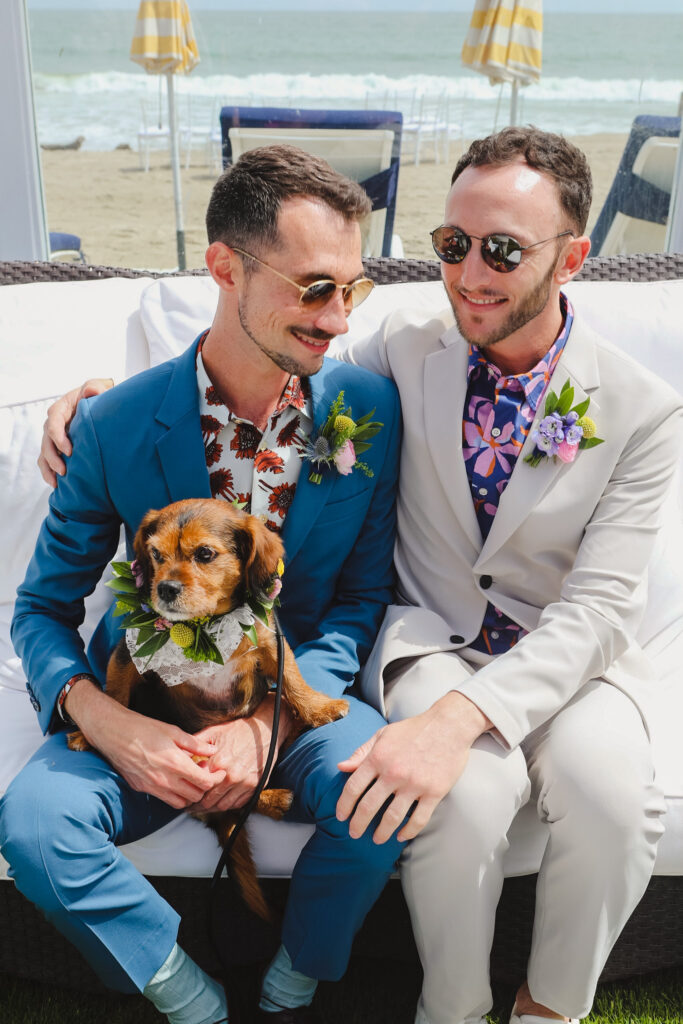 groom in bold print shirt and blue suit and groom in bold print shirt with tan suit hold dog with flower collar 