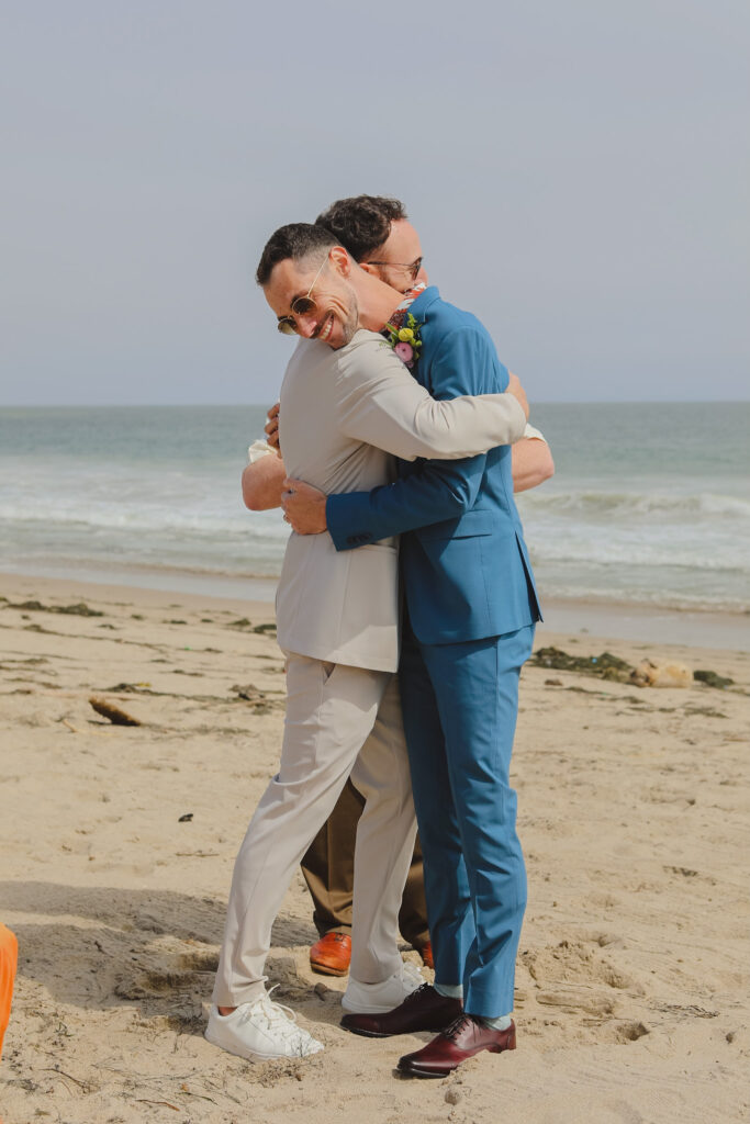 grooms embracing during private beach wedding ceremony