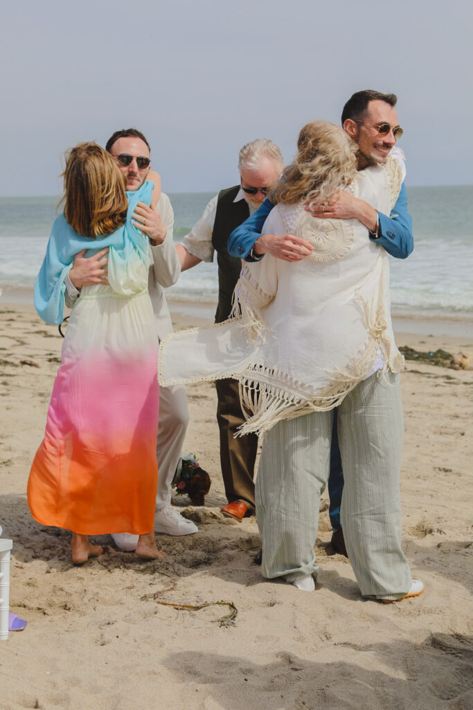 grooms embracing their mothers during private beach wedding ceremony