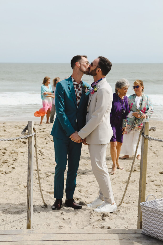 two grooms kiss after their wedding ceremony on the beach