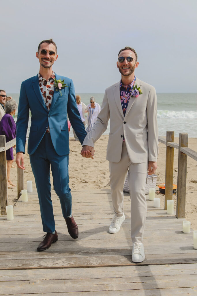 two grooms hold hands for recessional after their wedding ceremony on the beach
