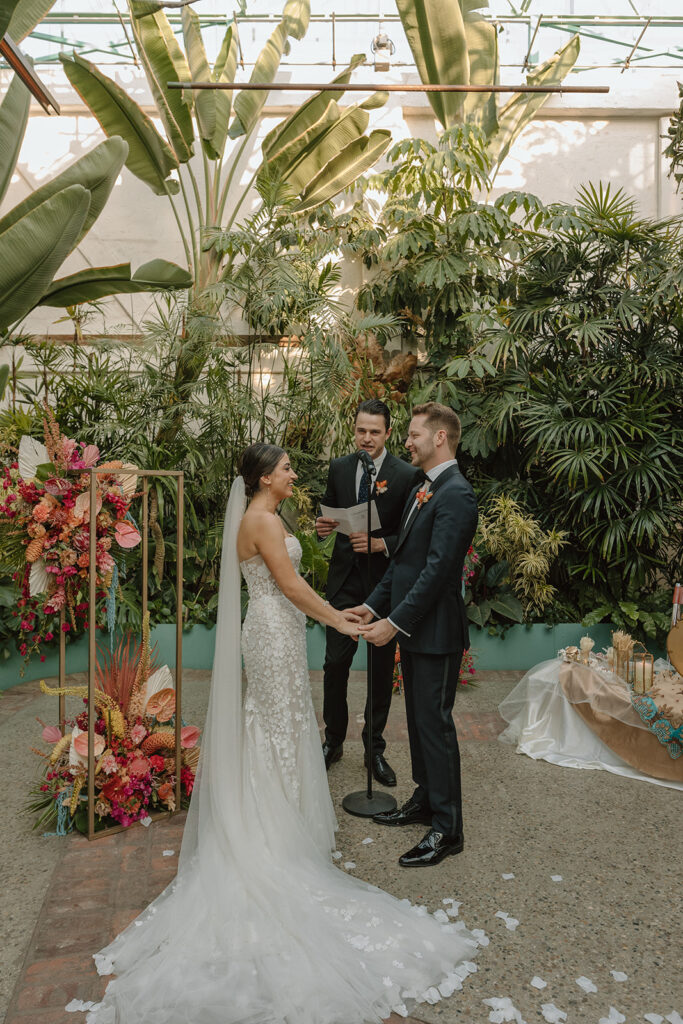 bride in strapless wedding dress with 3d floral appliqué stands with groom in black tuxedo during joyous wedding ceremony at Valentine DTLA