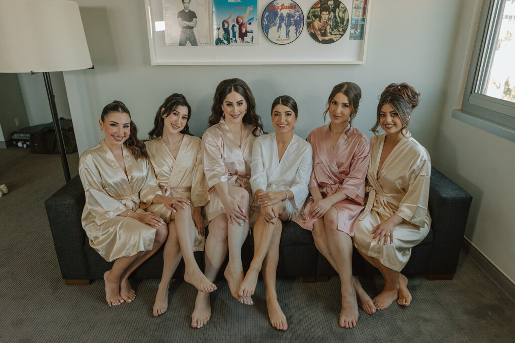 bride in white satin robe sitting with bridesmaids in champagne and pink satin robes