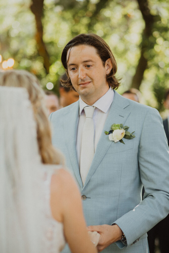 groom in light blue suit looking at bride in veil 