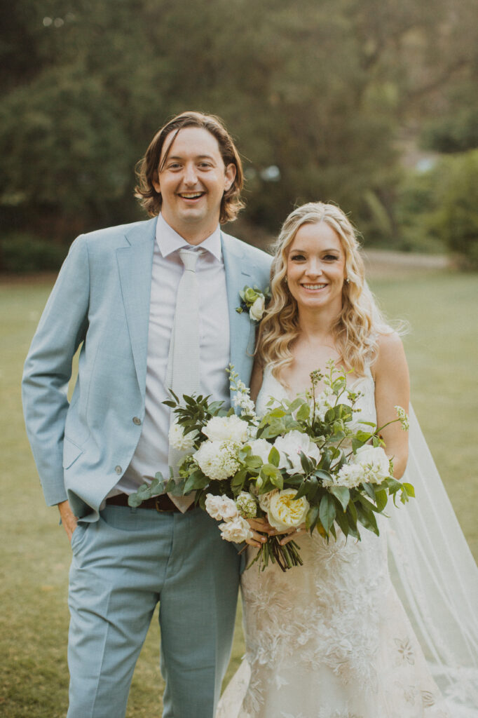 bride in lace wedding dress and white floral bouquet with groom in light blue suit at Calamigos Ranch for their soft gold summer wedding in Malibu 
