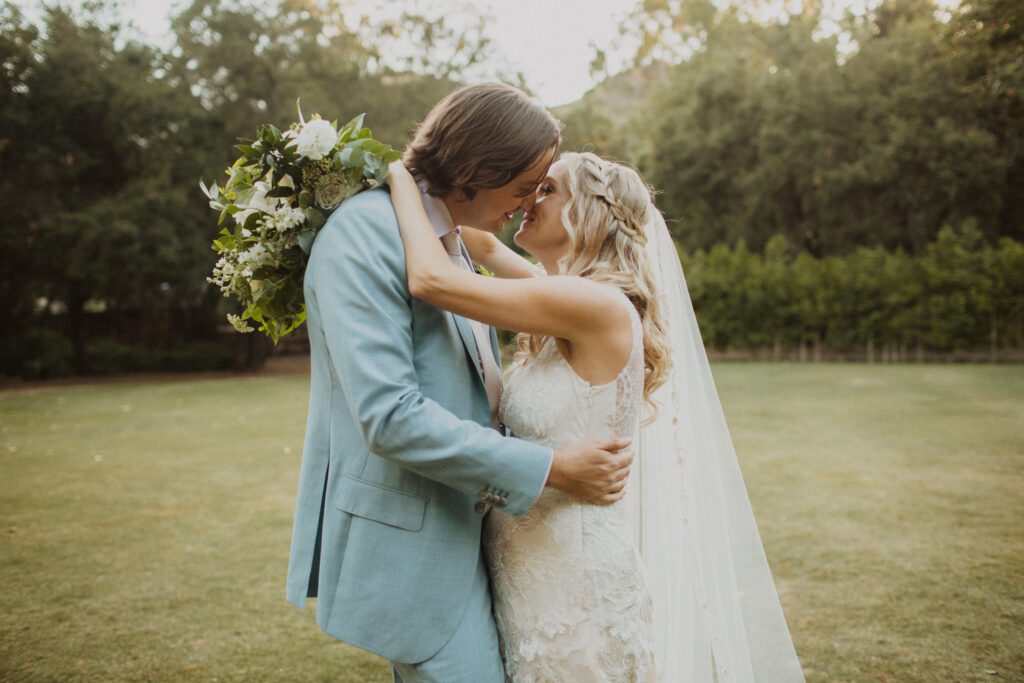 groom in light blue suit with bride in lace wedding dress and cathedral veil