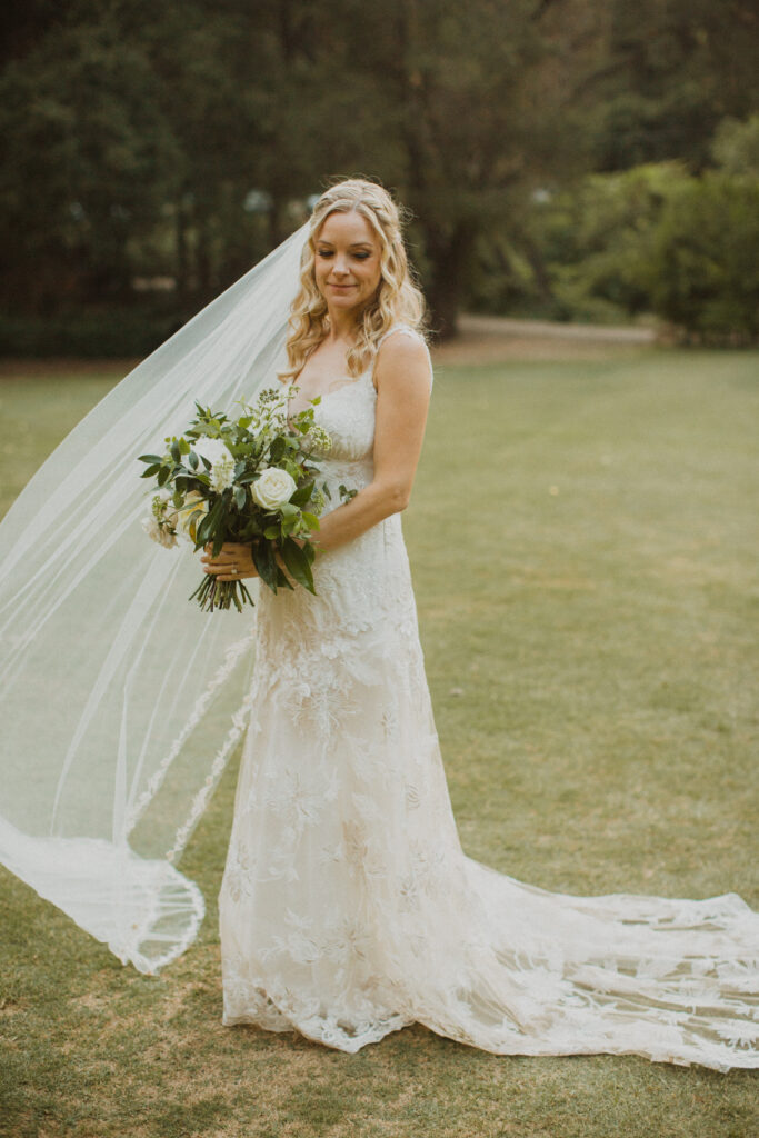 bride in lace wedding dress with floor length veil holding white floral bouquet