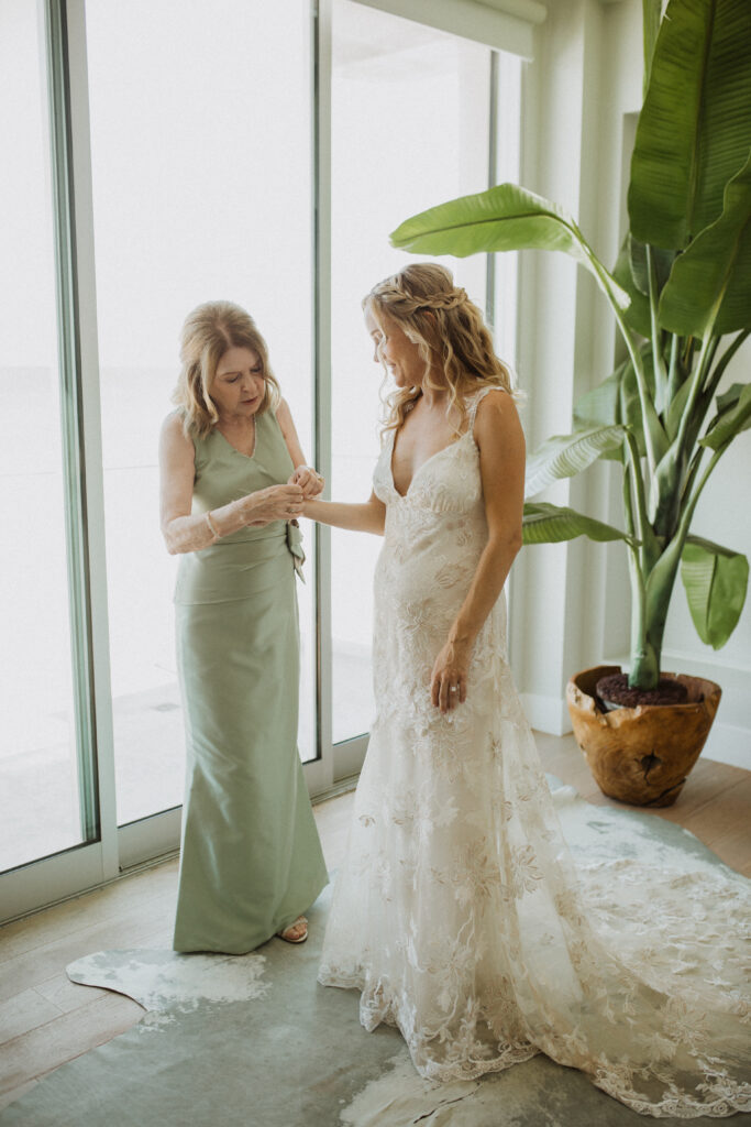 bride in lace wedding dress getting ready with mother of the bride in a green dress