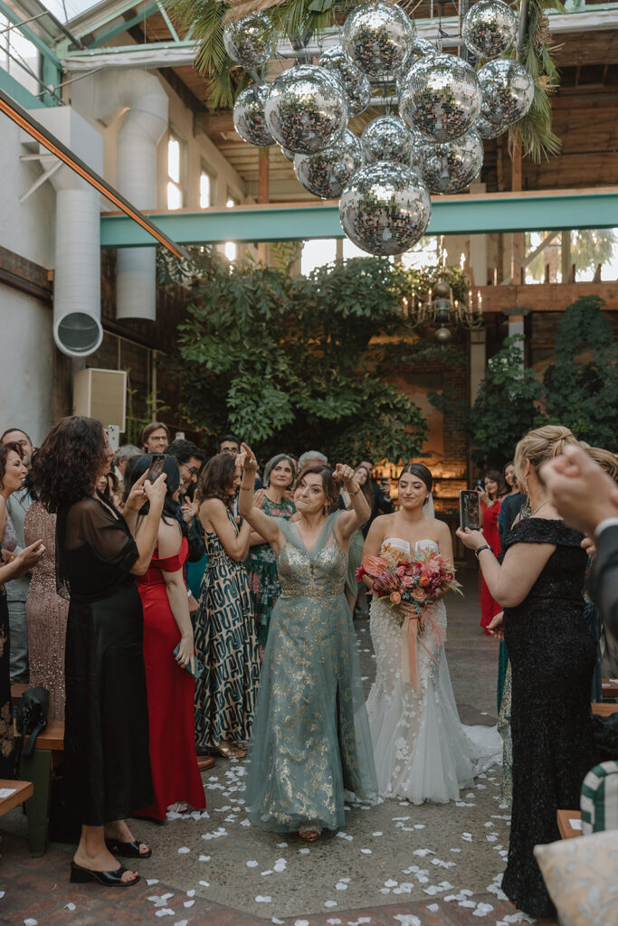 bride in strapless wedding dress with 3d floral appliqué dances with mother of the bride down ceremony aisle with hanging disco ball installation