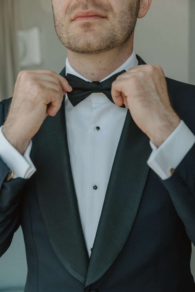 groom in black tuxedo with black bowtie getting ready for wedding