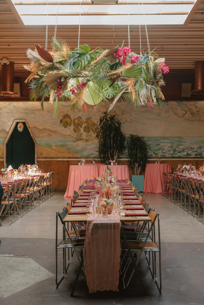 wedding reception at Valentine with large tropical floral hanging installation and pink table runner with pink dried floral arrangements
