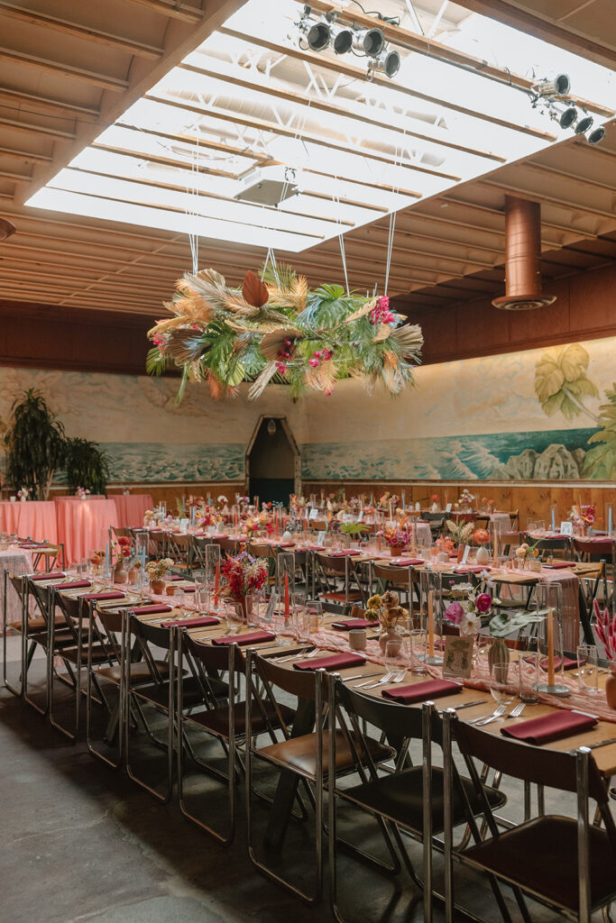 wedding reception at Valentine with large tropical floral hanging installation and pink table runner with pink dried floral arrangements