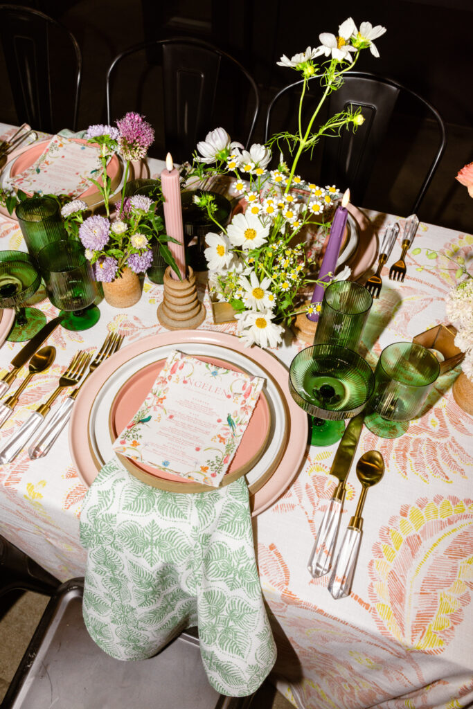 colorful summer dinner table decor with green glassware, taper candles,  wooden plates, floral table cloth and napkins and fresh floral centerpieces 
