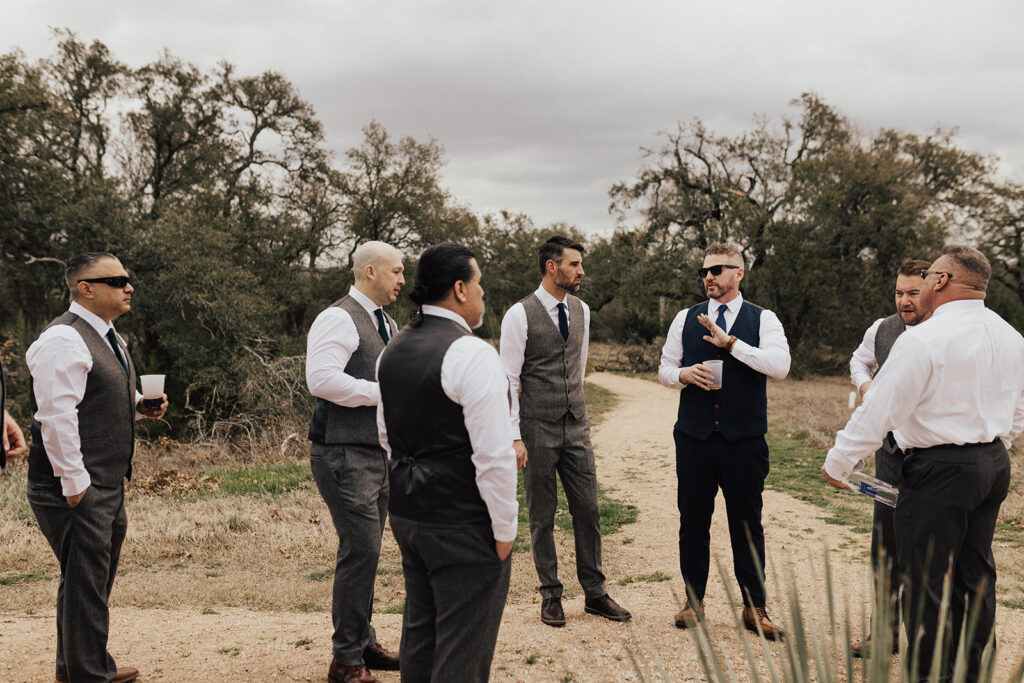 groom in navy vest talking with groomsmen in dark grey suits