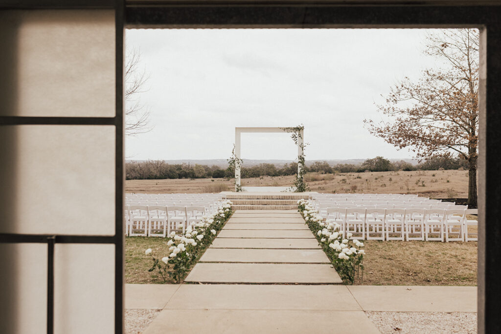 winter destination wedding at Prospect House in TX with frame wedding ceremony arch and white roses along aisle