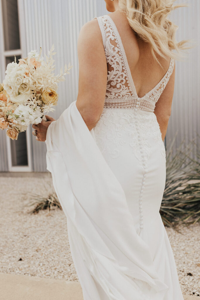 bride in deep v-neck wedding dress with lace elements and white rose bouquet stands in front of Prospect House before destination wedding