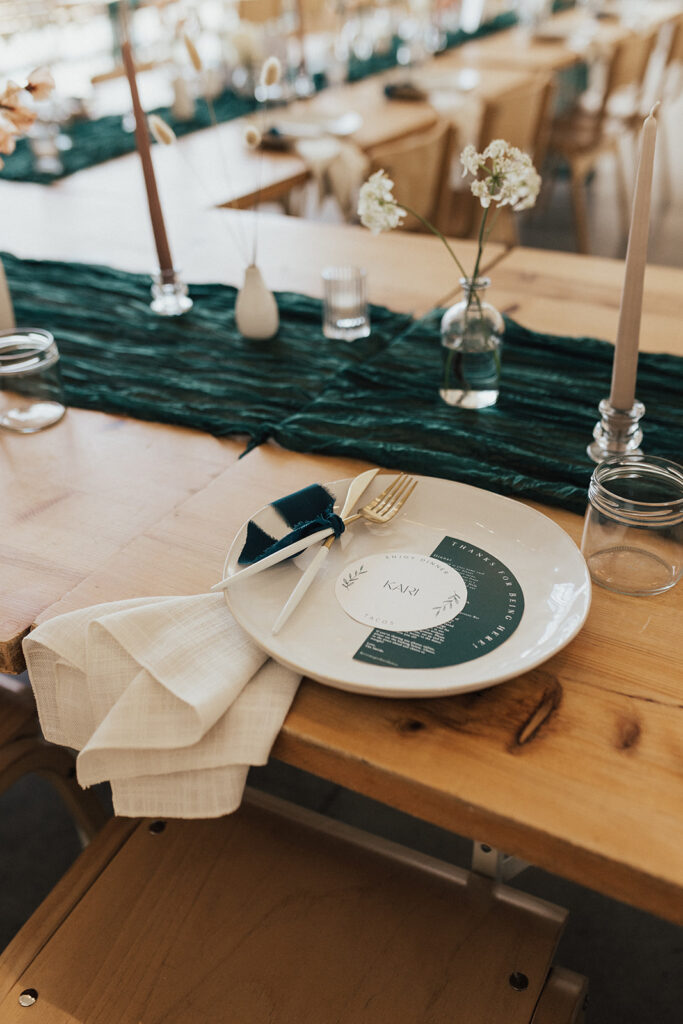 contemporary wedding reception with oak table and chairs, dark green gauze table runner and beige taper candles